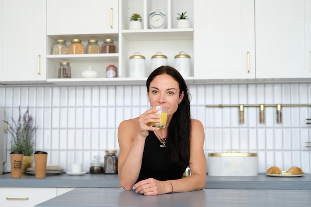 Een vrouw staat na een training thuis in een trainingspak in de keuken en drinkt sap uit een glas