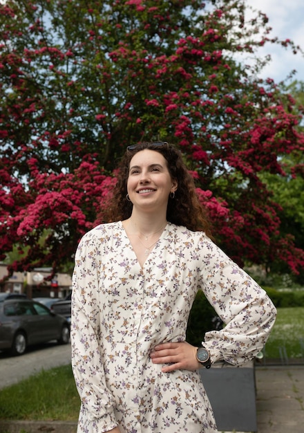 Een vrouw staat voor een boom met roze bloemen op de achtergrond.