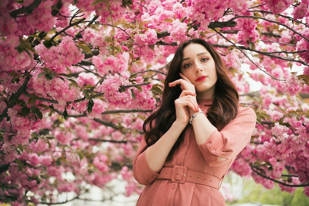 Een vrouw staat voor een boom met roze bloemen.