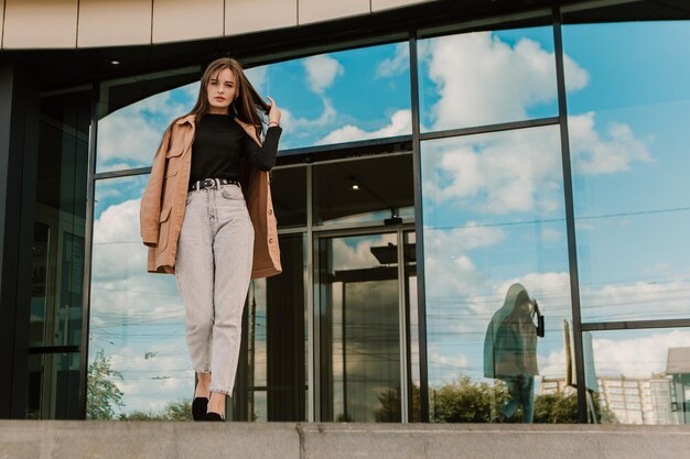 Een vrouw staat voor een glazen gebouw met een blauwe lucht achter haar