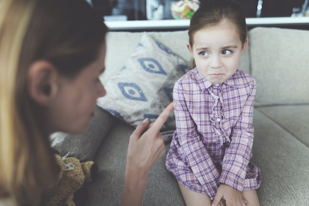 Een vrouw straft een meisje en trekt haar vinger grimassen.