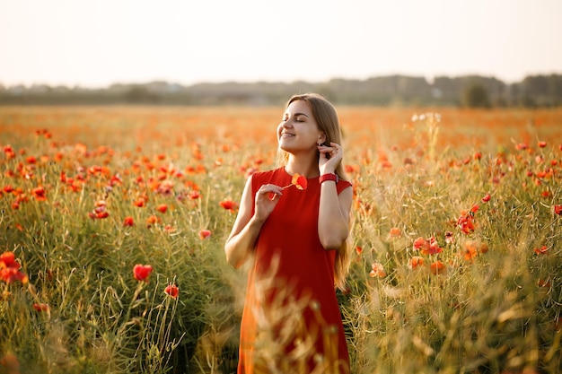 Een vrouw van Europees uiterlijk met lang blond haar en een rode zomerjurk, ze staat in een bloeiend papaverveld