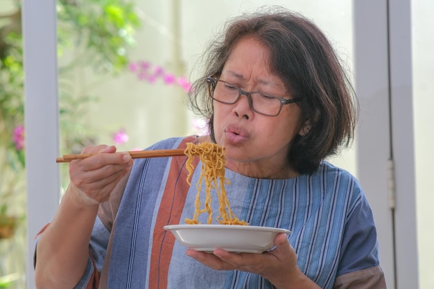 Een vrouw van middelbare leeftijd blaast op de noedels die ze gaat eten, zodat ze niet te heet worden