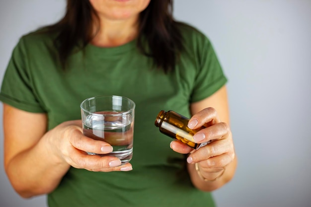 Een vrouw van middelbare leeftijd in vrijetijdskleding houdt thuis een pil en een glas vers water Hoofdpijn depressie medicijnen vitamines sedativa menopauze