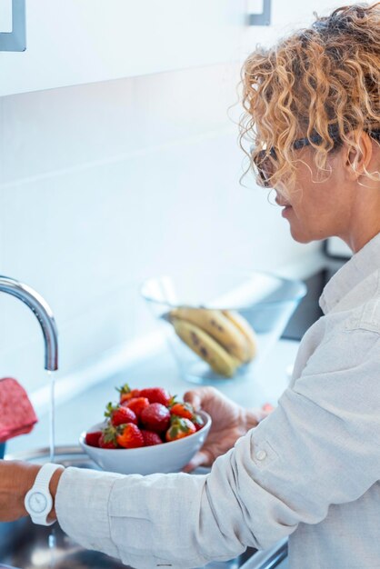 Een vrouw van middelbare leeftijd thuis met een verse schaal rode aardbeien seizoensgebonden fruit Concept van gewichtsverlies en calorie tekort telling Eten van natuurlijke dieet gezonde mensen vrouwelijke levensstijl aardbeien