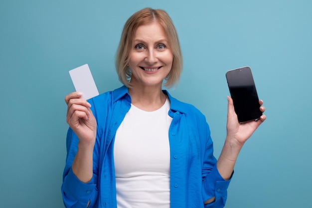 Een vrouw van volwassen jaren heeft een creditcard en een smartphone op een blauwe achtergrond kopieerruimte