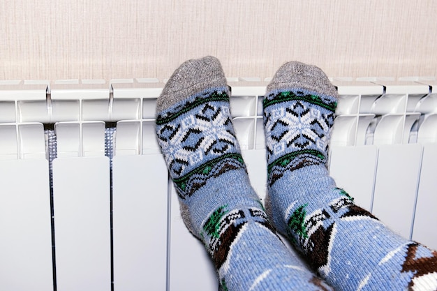 Een vrouw verwarmt haar bevroren voeten in sokken op een batterij het concept van warmte in huis koud seizoen