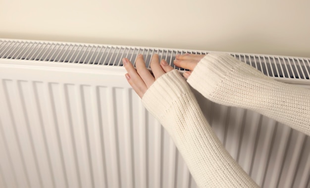 Een vrouw verwarmt haar handen op de radiator van de centrale verwarming van de huisclose-up