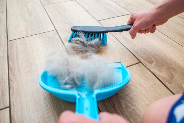 Een vrouw verwijdert hondenhaar nadat ze een hond heeft geschoren met een stofpannen en een bezem thuis