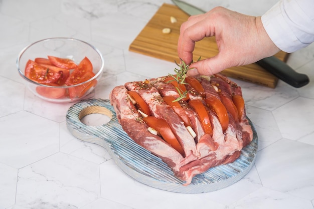 Een vrouw voegt een takje rozemarijn toe aan een rauwe varkensnek voordat ze gaat koken