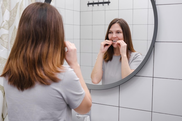 Een vrouw voor een spiegel in de badkamer die onzichtbare plastic tanden uitlijners of beugels aandoet