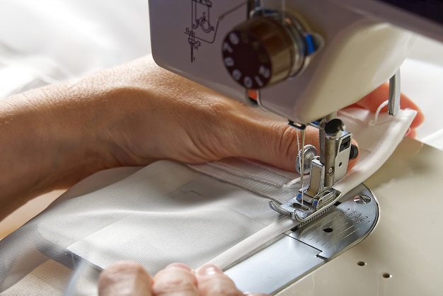 Een vrouw werkt op een naaimachine. naaister naait witte gordijnen, close-up.