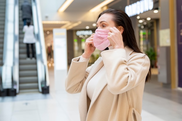 een vrouw zet een medisch beschermend masker op in een openbare ruimte