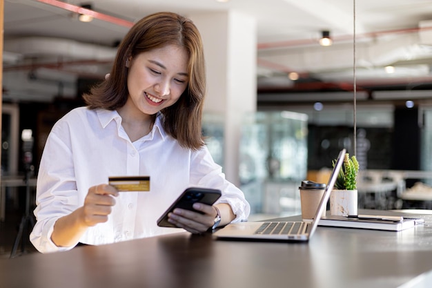 Een vrouw zit aan de balie met een mobiele telefoon en creditcard, ze winkelt online op een smartphone, ze betaalt voor goederen en diensten met een creditcard. Concept van het gebruik van creditcard voor betaling.