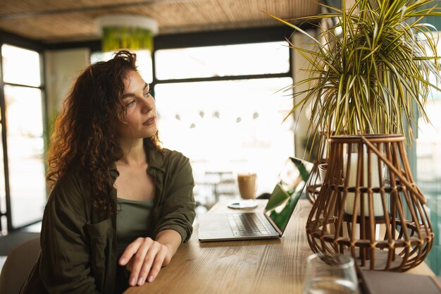 Een vrouw zit aan een tafel in een café en kijkt naar een laptop.