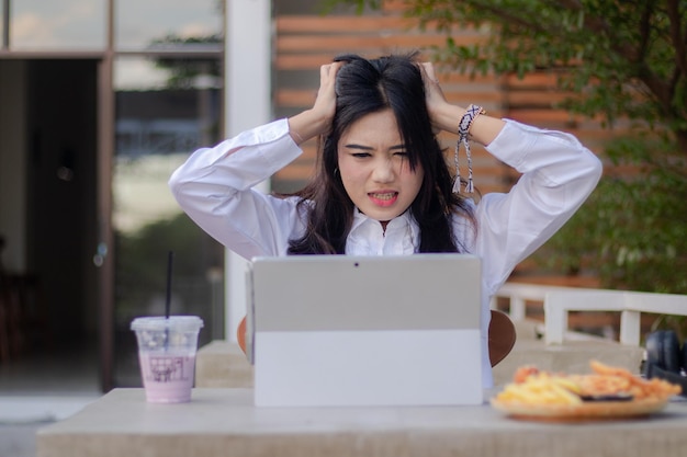 Een vrouw zit aan een tafel met een laptop en heeft haar handen op haar hoofd.