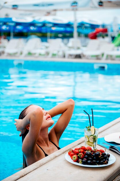 Foto een vrouw zit aan een tafel voor een zwembad met een bord eten en aardbeien.