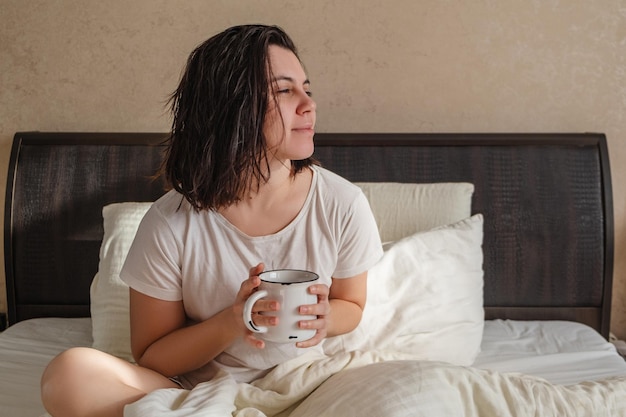 Een vrouw zit in bed met een mok koffie.