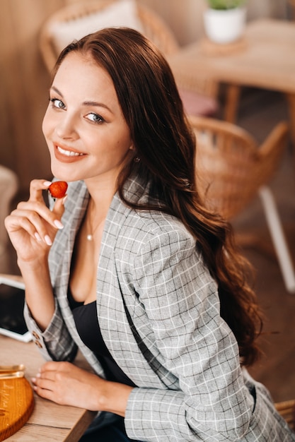 Een vrouw zit in een café en eet aardbeien. Een meisje met aardbeien in haar handen in een coffeeshop.