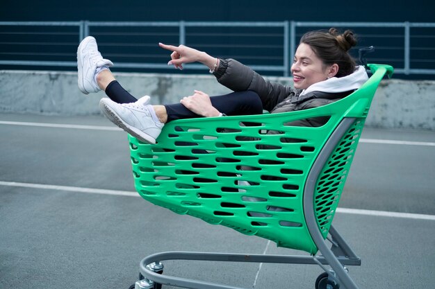 Een vrouw zit in een groen winkelwagentje en heeft een witte schoen aan.