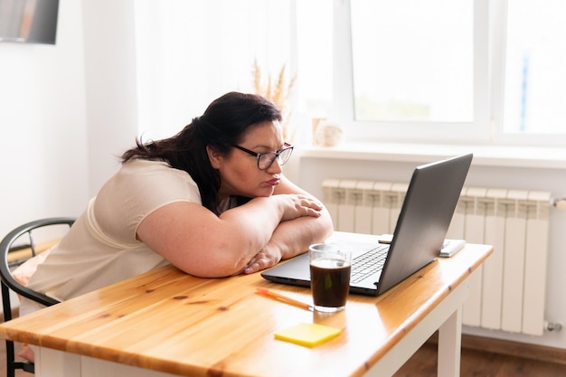 Een vrouw zit in een kamer aan een tafel met een laptop