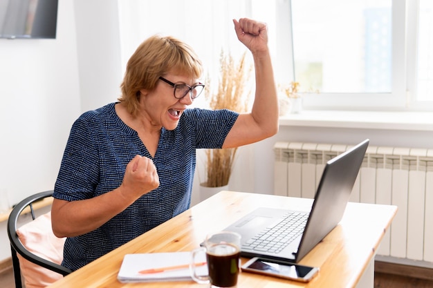 Een vrouw zit in een kamer aan een tafel met een laptop