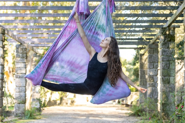 Een vrouw zit in een yogahangmat en strekt haar benen uit