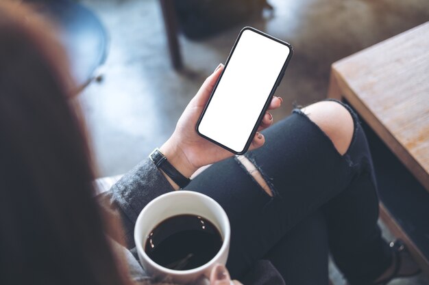 Een vrouw zit met gekruiste benen, houdt zwarte mobiele telefoon met leeg wit bureaubladscherm