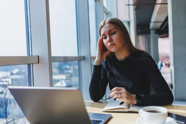 Een vrouw zit na een dag hard werken achter een laptop en houdt haar hoofd vast Hoofdpijn Migraine