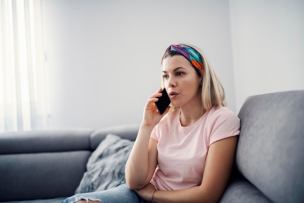 Een vrouw zit op de bank in haar gezellige huis en praat aan de telefoon