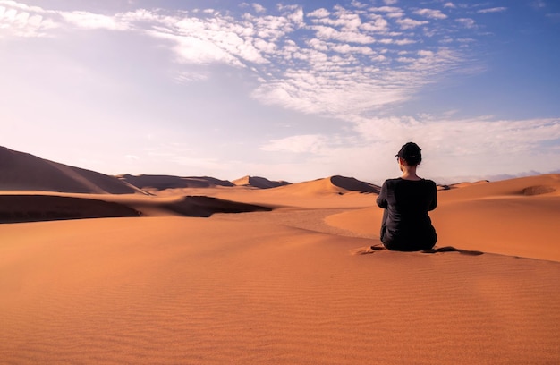 Een vrouw zit op de gouden zandduin van de Namib-woestijn