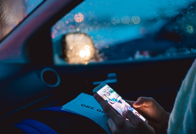 Een vrouw zit op de passagiersstoel van een auto en gebruikt een smartphone in de vroege winterochtend.