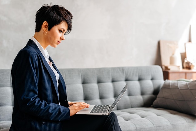 Een vrouw zit op een bank met een laptop op haar schoot.