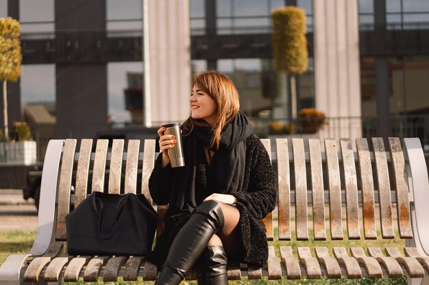 Een vrouw zit op een bankje in de stad en drinkt koffie en thermaalbekers