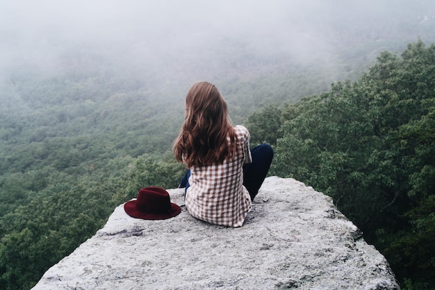 Foto een vrouw zit op een klif en kijkt uit over een vallei.