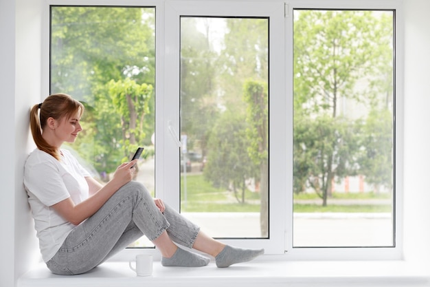 Een vrouw zit op een raam met een smartphone en schrijft