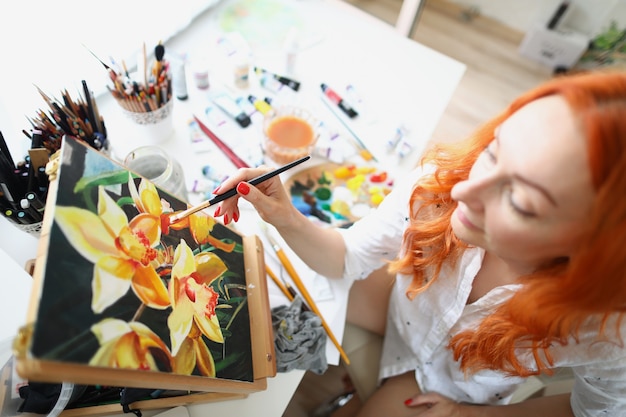 Een vrouw zit thuis voor een schildersezel en schildert bloemen gelukkige vrouwelijke kunstenaar in de