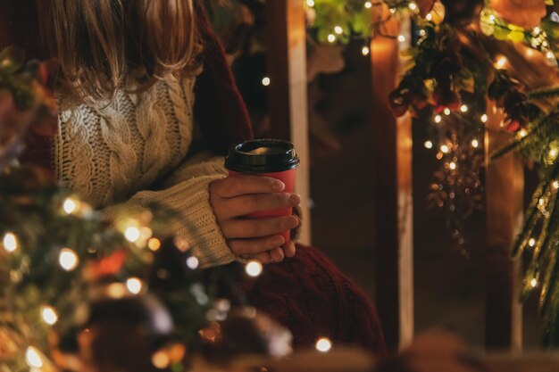 Een vrouw zit voor een kerstboom met een kopje koffie in haar hand.