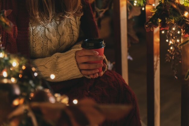 Een vrouw zit voor een kerstboom met een rode kop koffie.