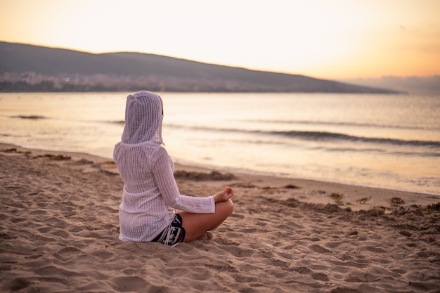 Foto een vrouw zittend op het zand in een lotus houding bij zonsopgang