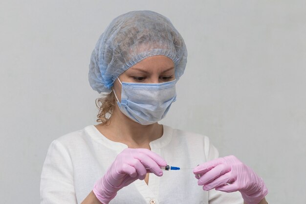 Een vrouwelijke arts, die handschoenen en een masker draagt, vult een spuit met medicijnen, close-up. Covid-19-vaccinatie