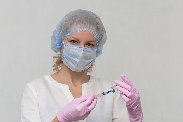 Een vrouwelijke arts, die handschoenen en een masker draagt, vult een spuit met medicijnen, close-up. Covid-19-vaccinatie