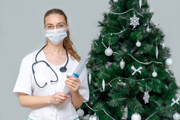 Een vrouwelijke arts in een beschermend medisch masker houdt een grote spuit vast
