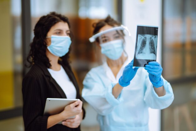 Een vrouwelijke arts in vizier en beschermende handschoenen onderzoekt een röntgenfoto van een patiënt