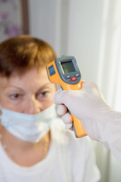 Een vrouwelijke arts meet de temperatuur van een volwassen vrouw met een laserapparaat