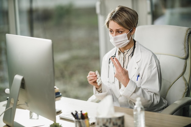 Een vrouwelijke arts met beschermend gezichtsmasker die online met de patiënt werkt tijdens de COVID-19-pandemie.