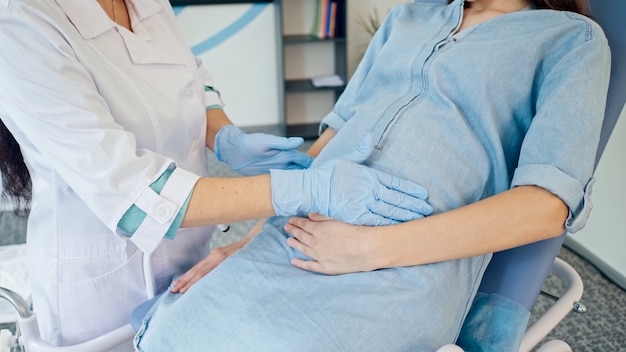 Een vrouwelijke arts onderzoekt een zwangere jonge moeder om haar gezondheid te controleren