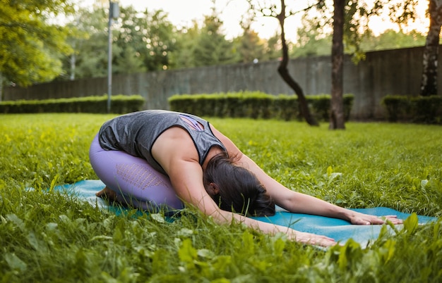 Een vrouwelijke atleet voert een yoga Balasana pose uit bij zonsondergang in een park