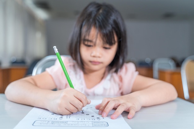 Een vrouwelijke aziatische studente concentreert zich op het examenpapier in de klas