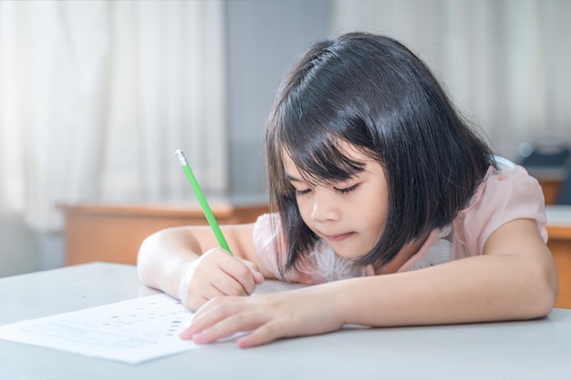 Een vrouwelijke Aziatische studente concentreert zich op het examenpapier in de klas